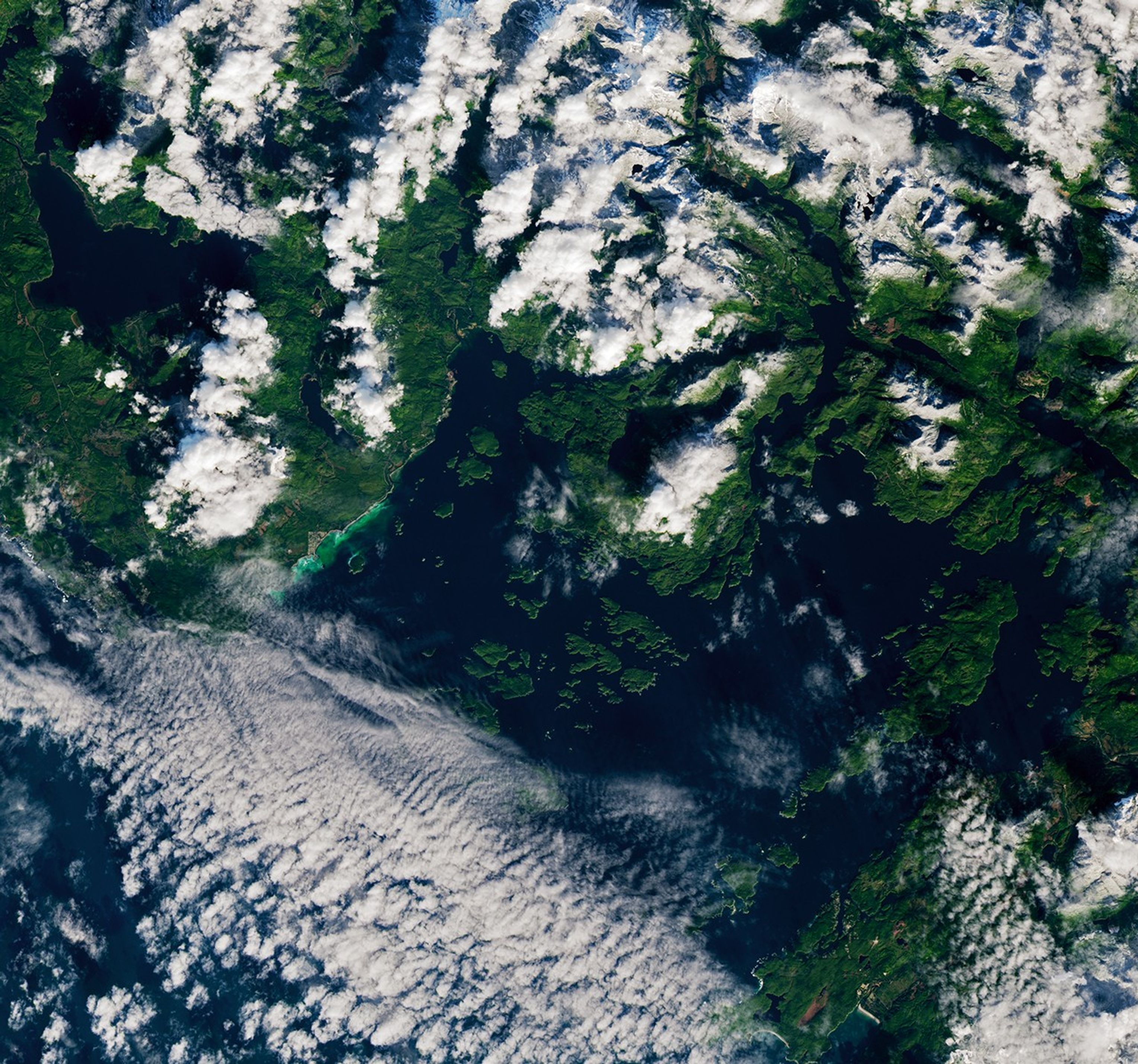A swath of water along the coast of Vancouver Island appears cloudy and green to turquoise in color.