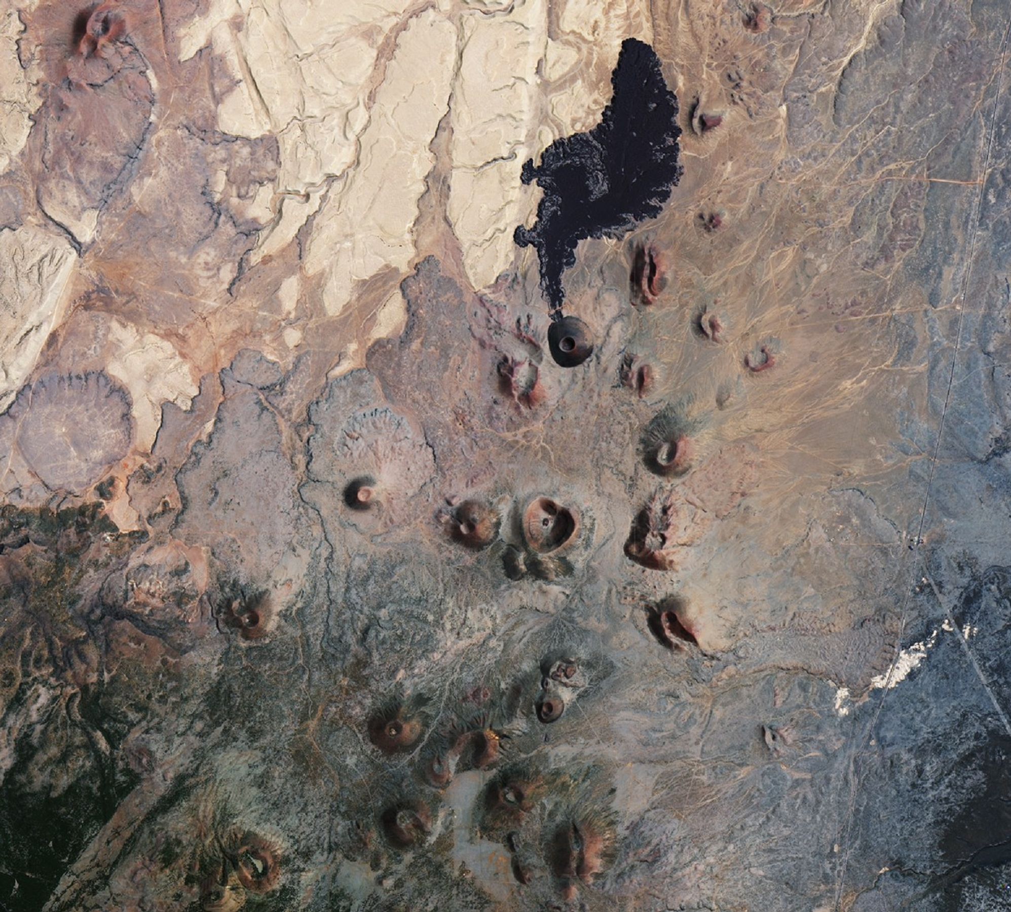 A downward-looking satellite image shows several reddish scoria cones in the San Francisco Volcanic Field in Arizona. The scoria cones look like small hills with circular vents. A darker-colored cone called SP Crater has a black lava flow extending northward from it.