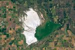 The Great Salt Plains in Oklahoma occupy a roughly triangular area surrounded by agricultural fields. Several streams run through an expanse of bright salt that covers the western side, and a lake with green-tan water fills the eastern corner behind a dam.