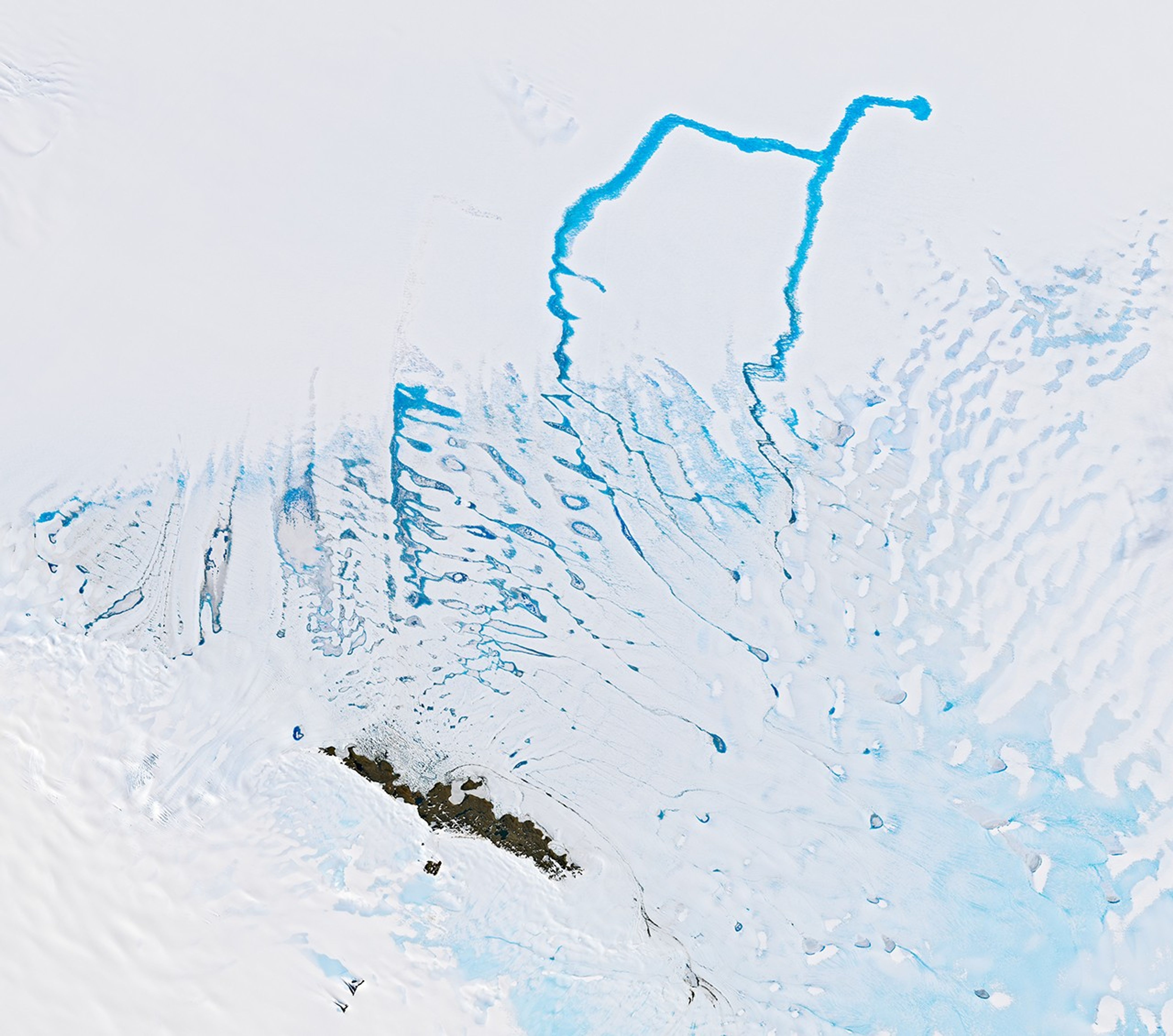 A network of cerulean blue meltwater drainage channels flowing across white and blue ice surfaces. An 