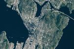 A top-down photo focuses on downtown Seattle, where tall buildings cast long shadows. Green neighborhoods and parks surround the dense urban development, and large waterbodies lie to the east and west.