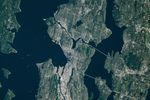 A top-down photo of the greater Seattle area shows a mix of light-colored developed areas and green parks and neighborhoods. Puget Sound and Lake Washington run along Seattle’s west and east sides, respectively.