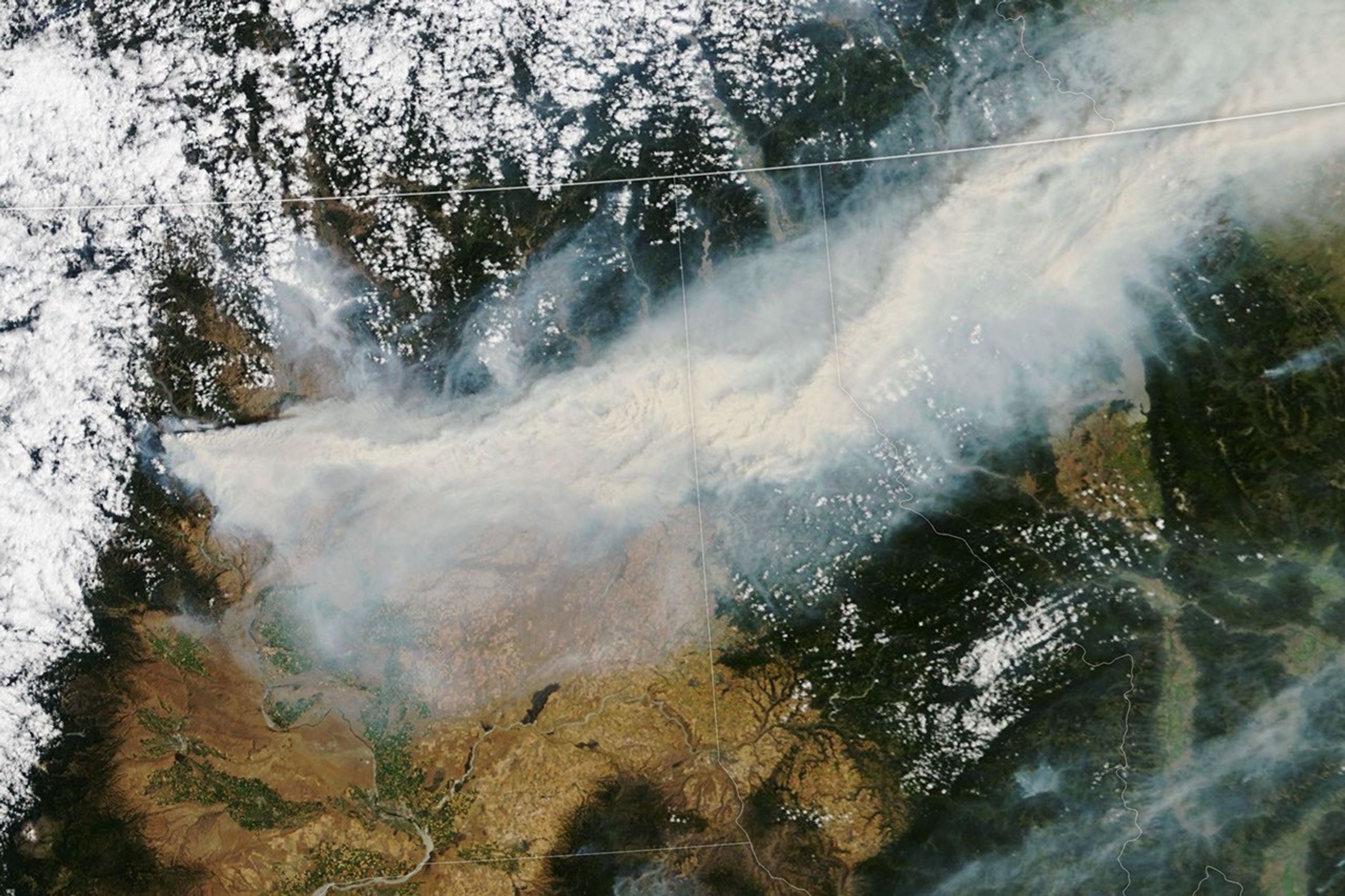 A wide plume of brown-gray smoke stretches across a satellite image spanning Washington, Idaho, Montana, and Canada.