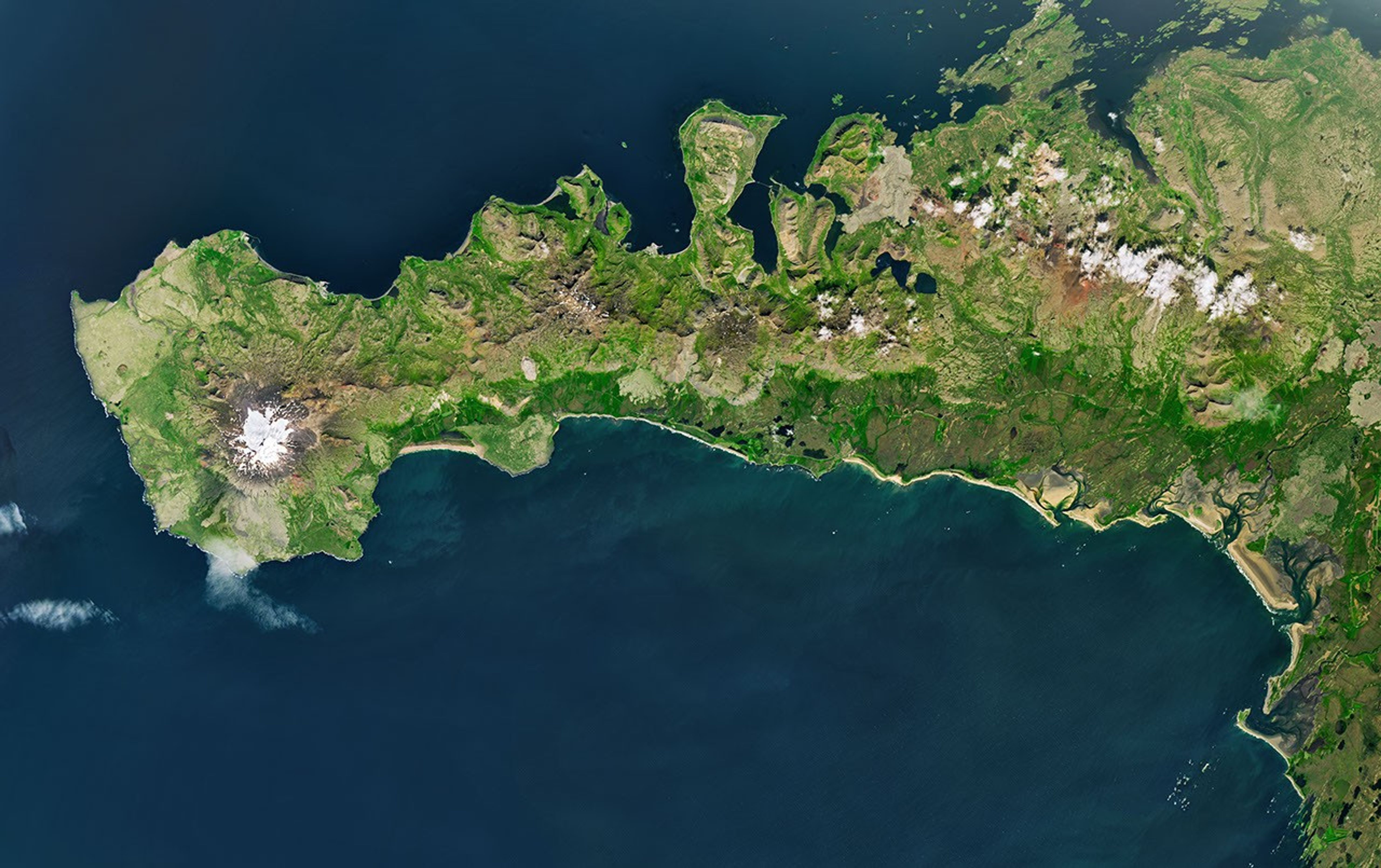 A peninsula in Iceland stretches across the image to the left. A prominent glacier-capped volcano sits near its western end.