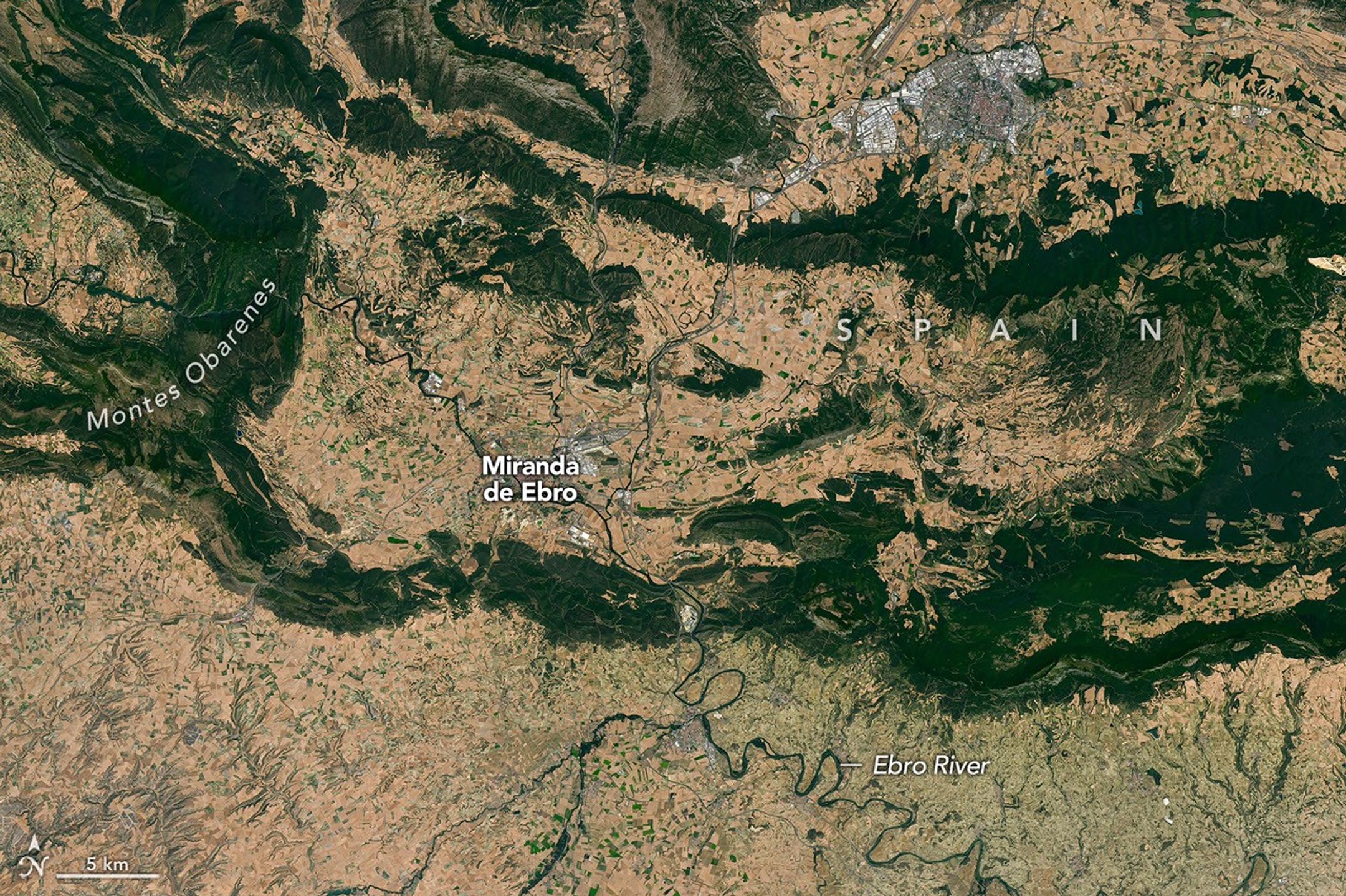 Meandering rivers cut through dark green mountain ridges, across agricultural land, and near several developed areas in northern Spain.