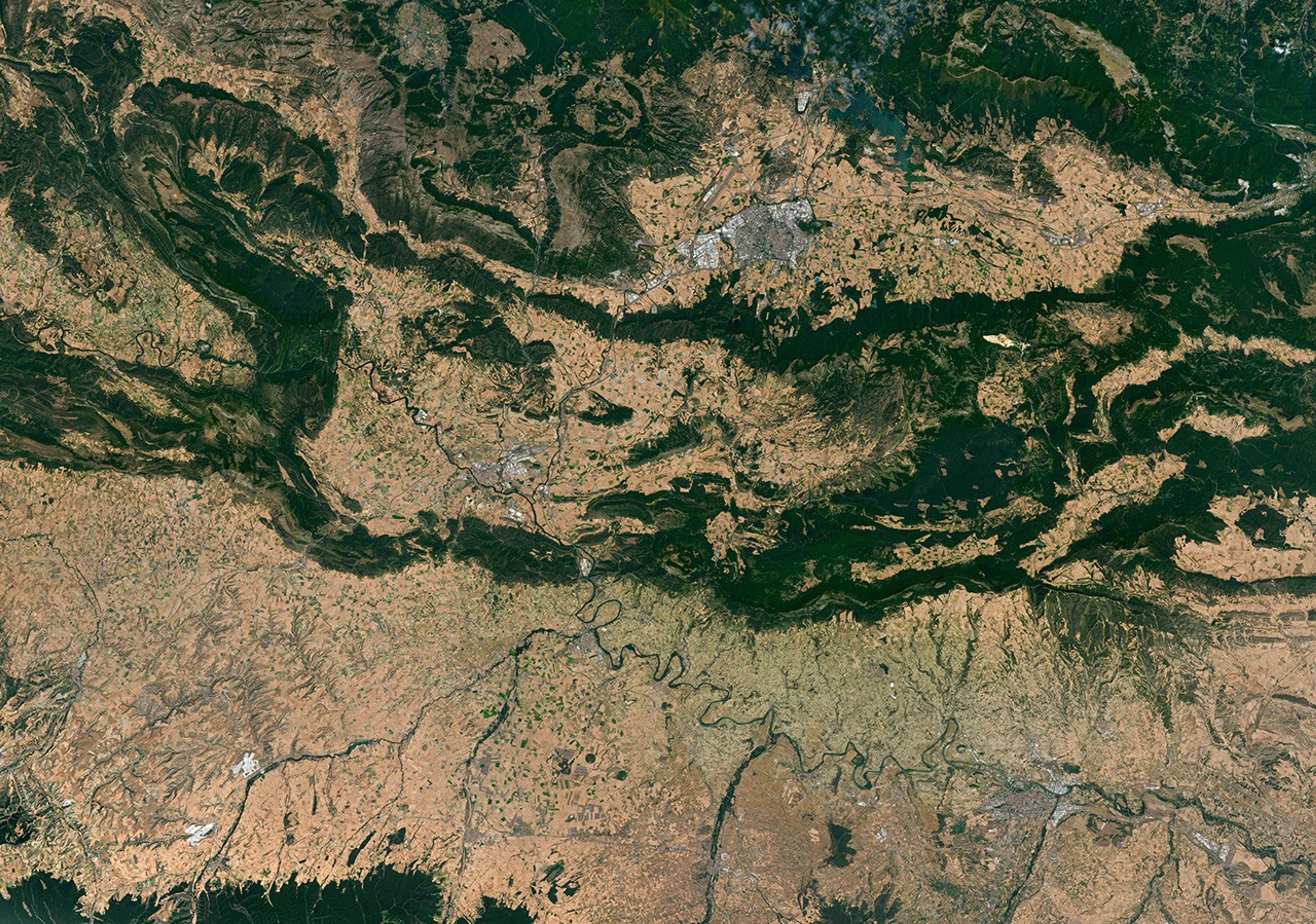 Meandering rivers cut through dark green mountain ridges, across agricultural land, and near several developed areas in northern Spain.