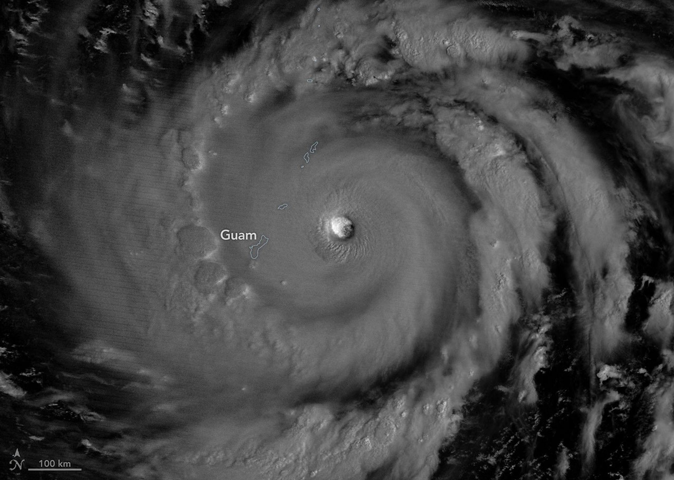 The eyewall of a super typhoon is partially illuminated by moonlight in a nighttime satellite image.