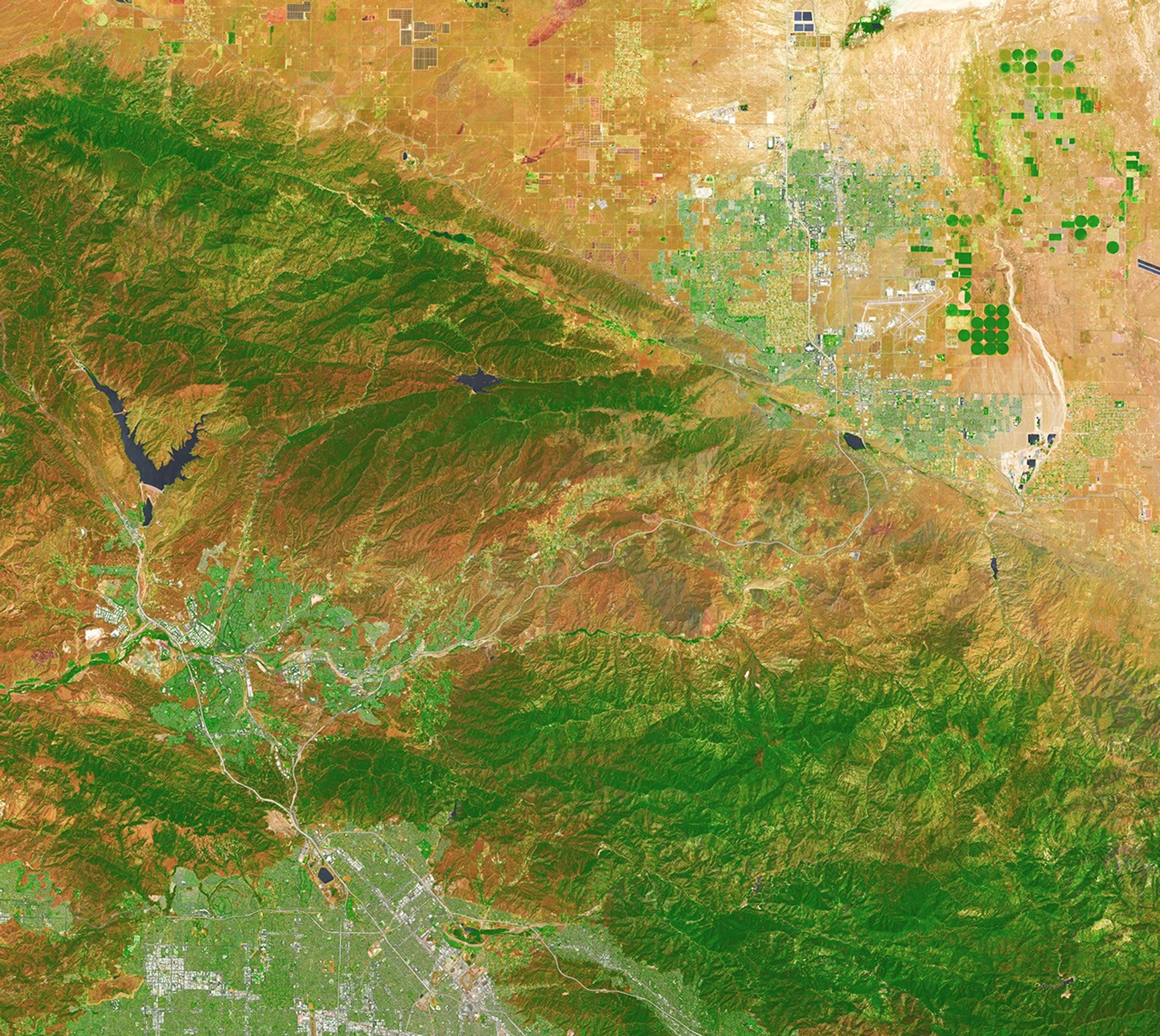 In this false-color image, areas with more extensive vegetation on the Sierra Pelona retain more moisture than the hills surrounding Agua Dulce, making the Sierra Pelona appear dark green in comparison to the rusty brown coloration of the lower hills. Vasquez Rocks appears as a patch of curved gray stripes near the center of the image.