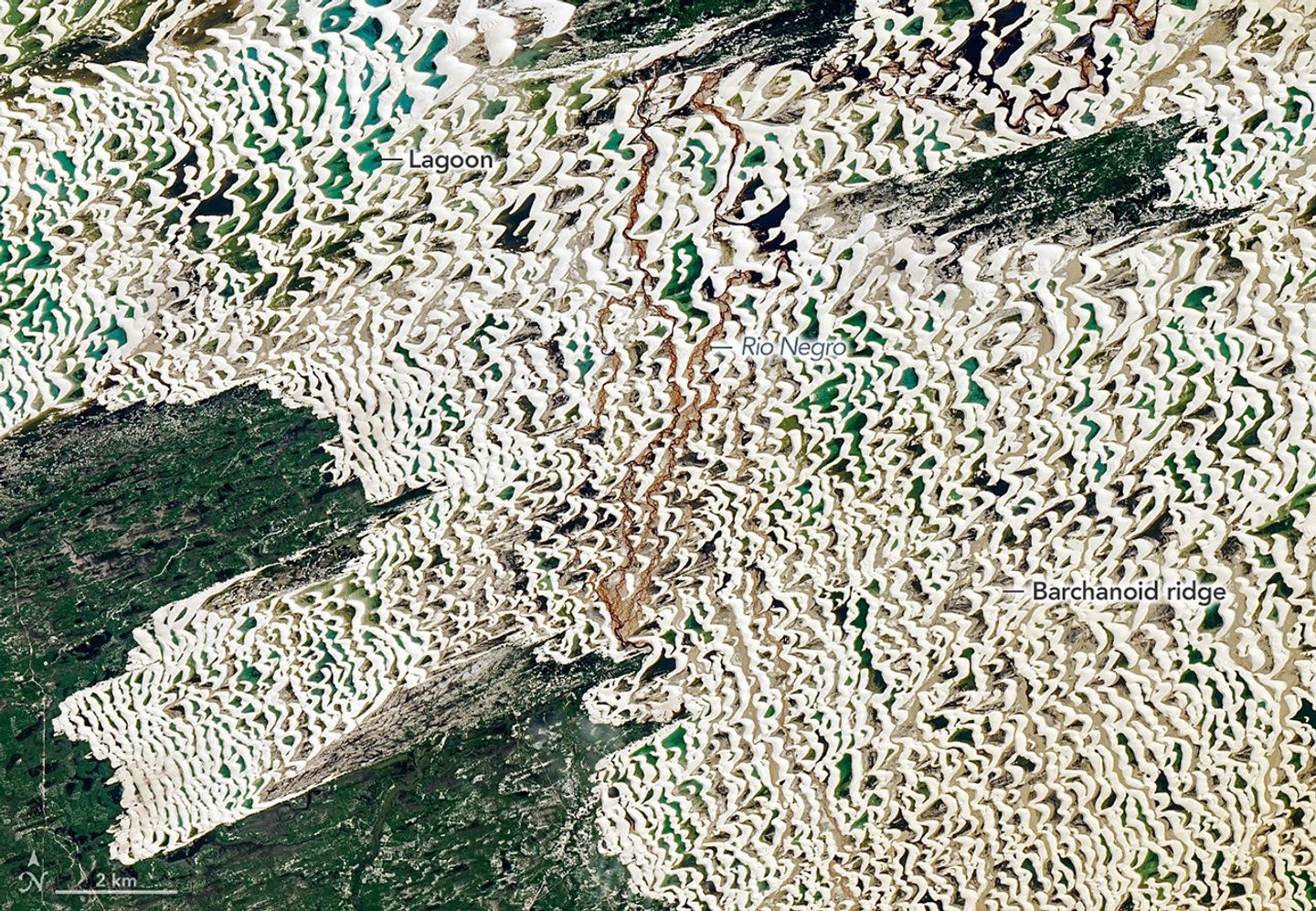 The various blue and greens of the lagoons are more visible in this view of a portion of the dune field. A small river with brown water is visible running northward through the dune field.