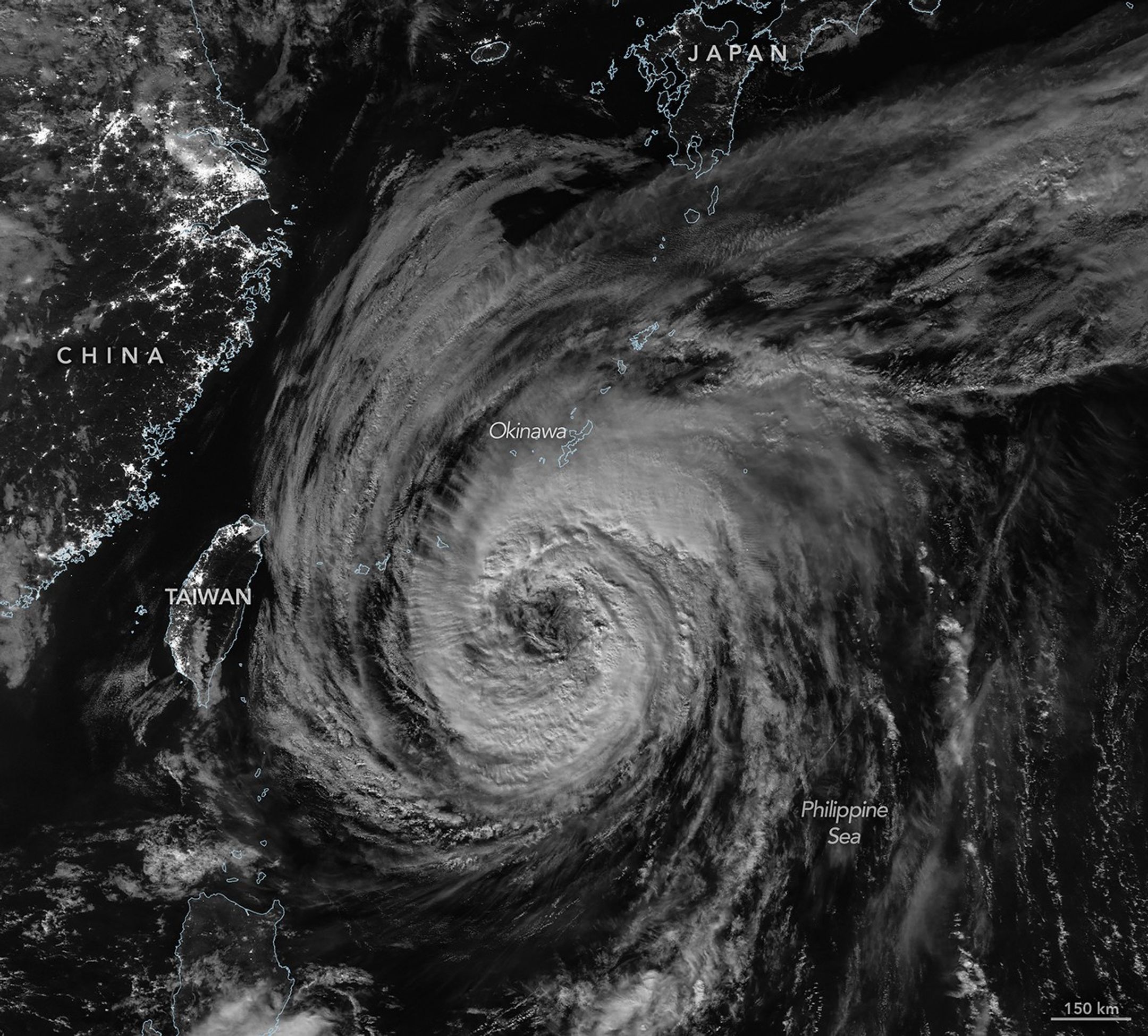 A nighttime satellite image shows a wide view of the typhoon with its outer cloud bands extending over southern Japan.
