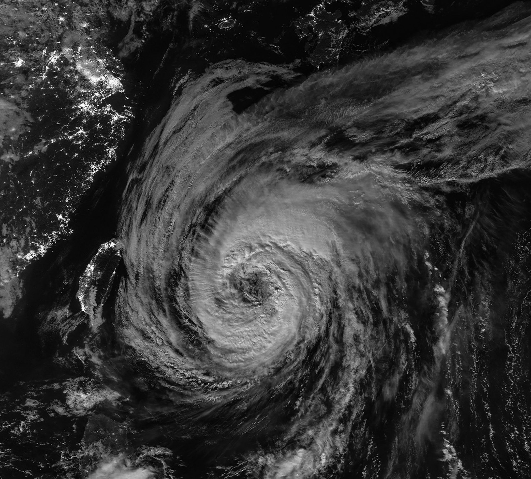 A nighttime satellite image shows a wide view of the typhoon with its outer cloud bands extending over southern Japan.