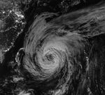 A nighttime satellite image shows a wide view of the typhoon with its outer cloud bands extending over southern Japan.
