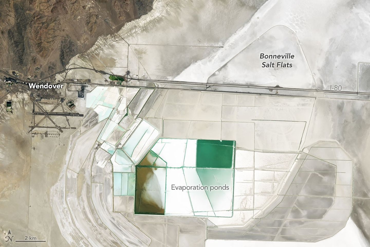 Straight roads, colorful evaporation ponds, and a long racetrack are visible on bright white salt flats in a satellite image centered east of Wendover.