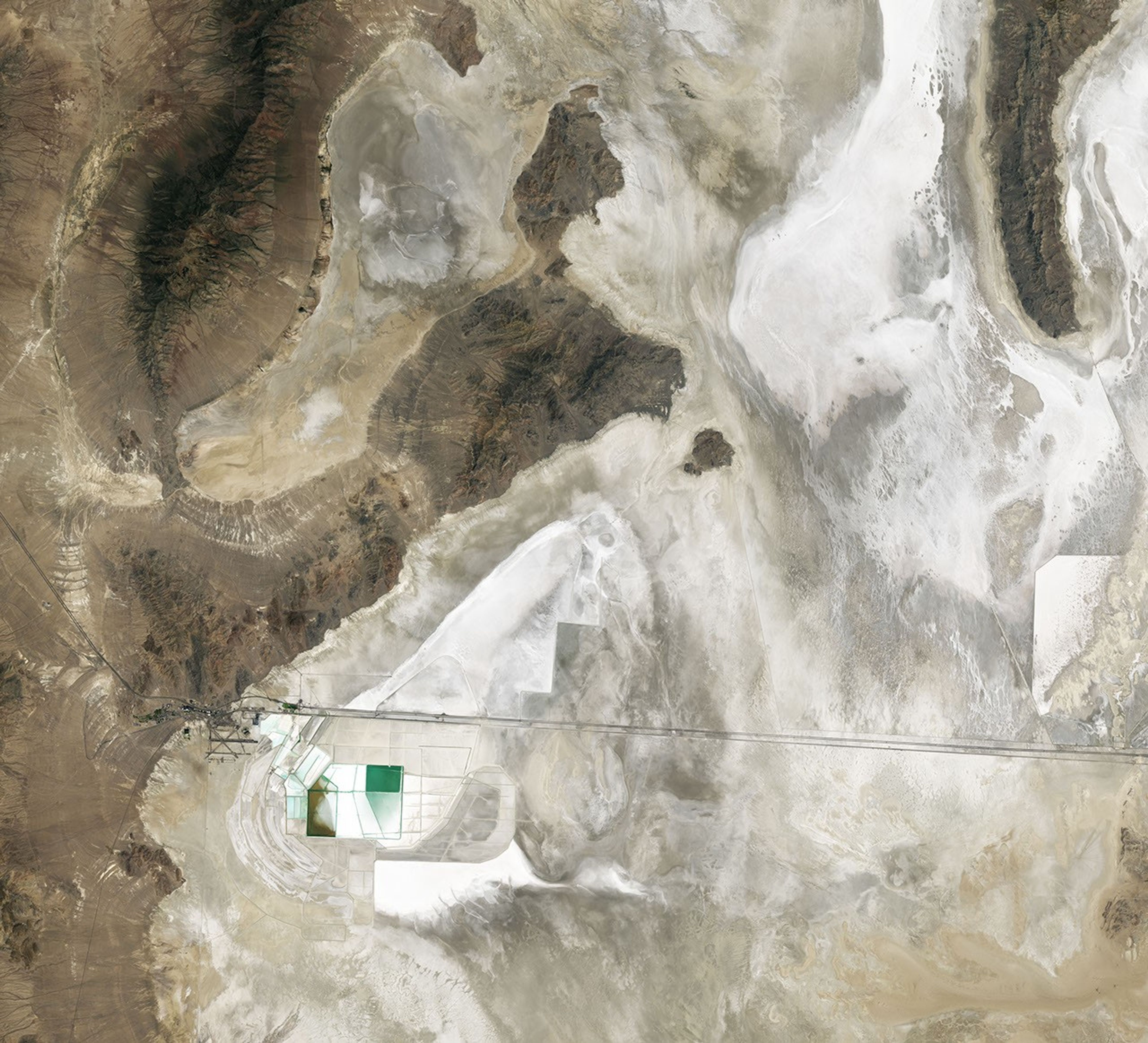 A nadir view shows Crater Island—a dark, linear mountain ridge in the center of the image—flanked by flat tan and white landscapes.