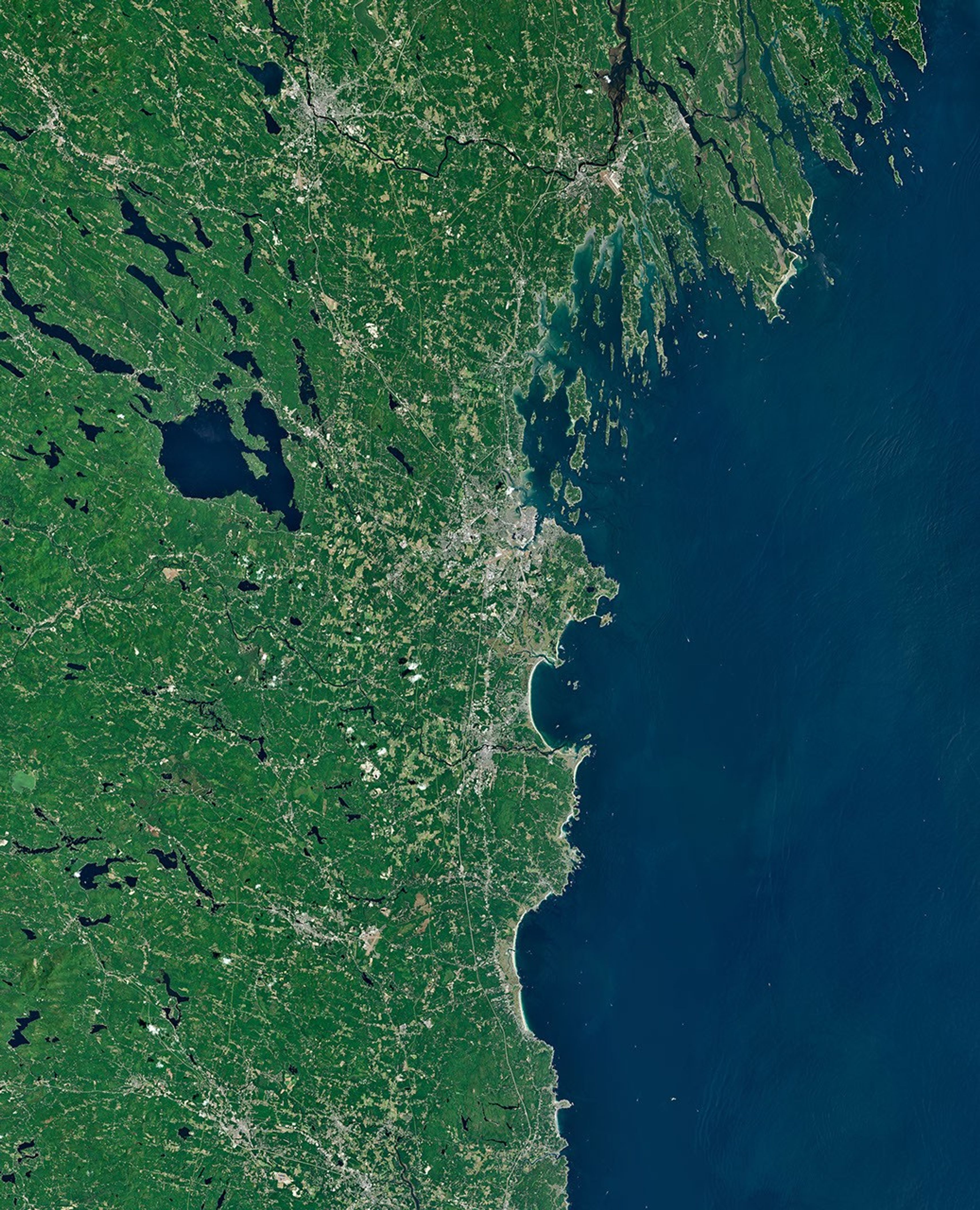 A satellite image of the Maine coastline highlights smooth, sandy beaches near Saco Bay on the left and the rocky, jagged coastal features near Casco Bay on the right.