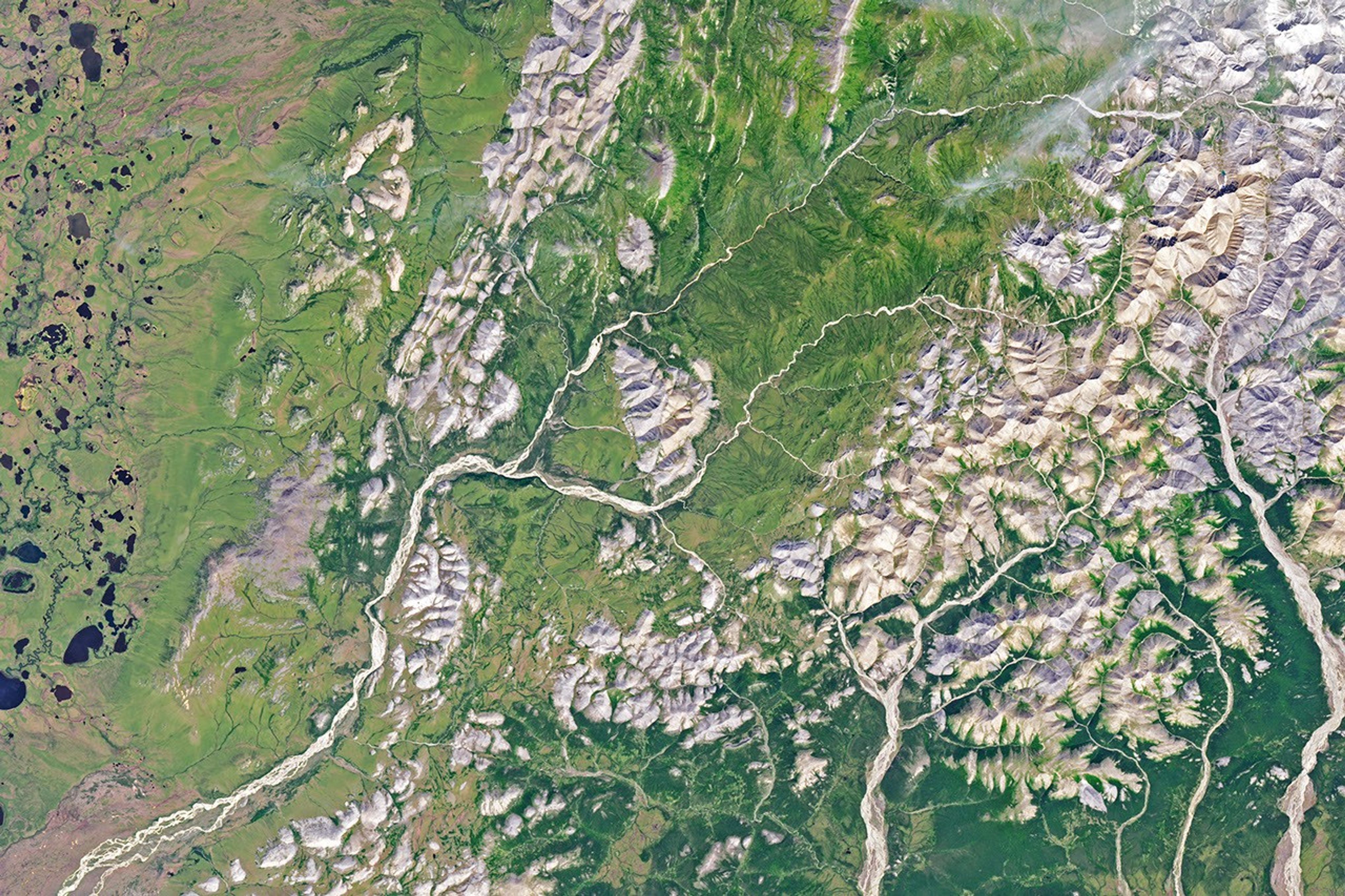 A gently curving river runs from right to left through green tundra vegetation. A segment of the river appears orange.