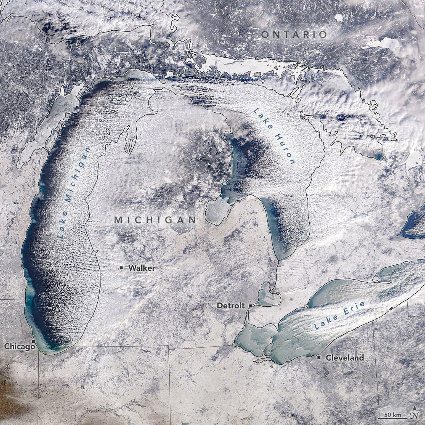 A satellite view of the Great Lakes shows a winter landscape, with snow-covered land, ice forming on parts of the lakes, and clouds trialing over open water.