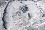 A satellite view of the Great Lakes shows a winter landscape, with snow-covered land, ice forming on parts of the lakes, and clouds trialing over open water.
