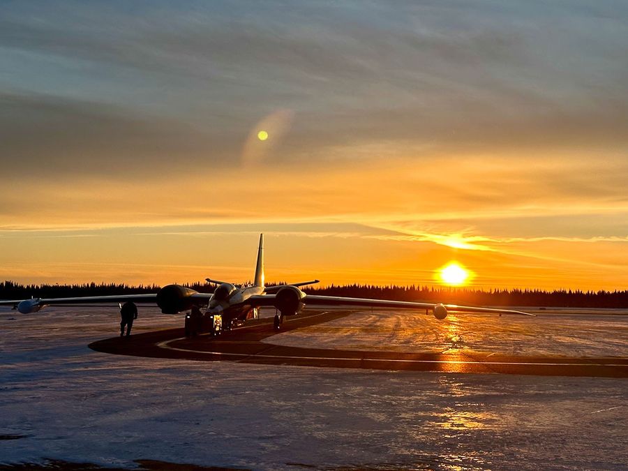 Two people walk in front of an airplane sitting on a snow covered runway. at sunset.