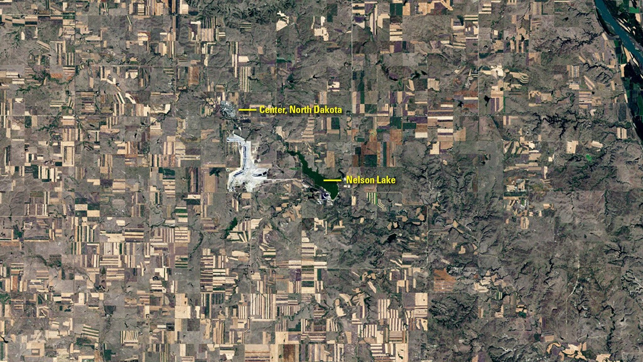 Mining has been part of Center, North Dakota’s history for over a century. The Landsat 5 image from August 1984 (left) shows significant surface mining of lignite coal just to the southeast of town, during a summer when drought had browned the countryside. Thirty-two years later, mining activity moved to the southwest of Center. An additional mining operation also began near the Milton R. Young Power Plant just southwest of Nelson Lake, where lignite is used to heat water and create steam to drive electricity-producing turbines. The North Dakota Geological Survey estimates that western North Dakota contains about 1.3 trillion tons of lignite, and that 25 billion tons are recoverable—enough to last more than 800 years at the current production rate of 30 million tons per year. Left image taken by the Landsat 5 satellite. Right image taken by Landsat 8. Source: U.S. Geological Survey (USGS) Landsat Missions Gallery: “Landsat Monitors Mining at Center of North America Near Town of Center”; U.S. Department of the Interior / USGS and NASA.