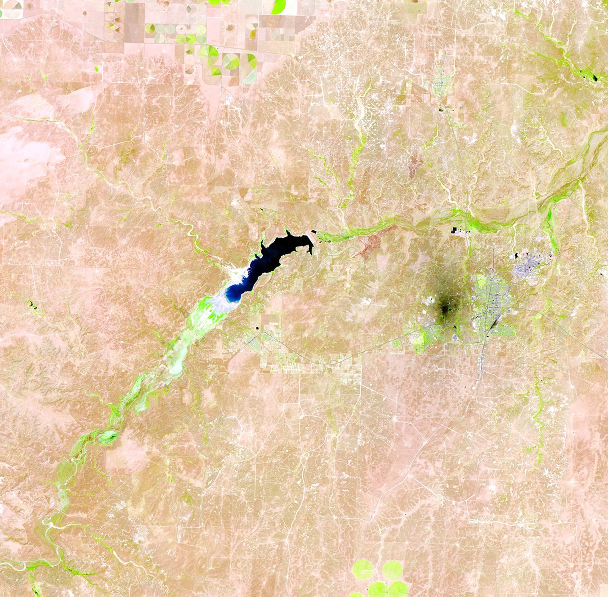 Lake Meredith is a reservoir formed by the Sanford Dam on the Canadian River in the Texas panhandle. Continuous drought has diminished water levels significantly in the past few years, leading to a record low in 2011. In each image, the lake is the black feature near the center. Light tones at the lower end of the lake indicate dry land and former shores. Bright green indicates healthy vegetation along the river beds and irrigated fields in the upper center of each image. The nearby industrial area (a petroleum plant and a carbon-processing plant) appears as a dark spot. The light blue tone further east is Borger, Texas. Images taken by the Thematic Mapper sensor aboard Landsat 5. Source: USGS Landsat Missions Gallery, "Shrinking Lake Meredith, Texas," U.S. Department of the Interior / U.S. Geological Survey.