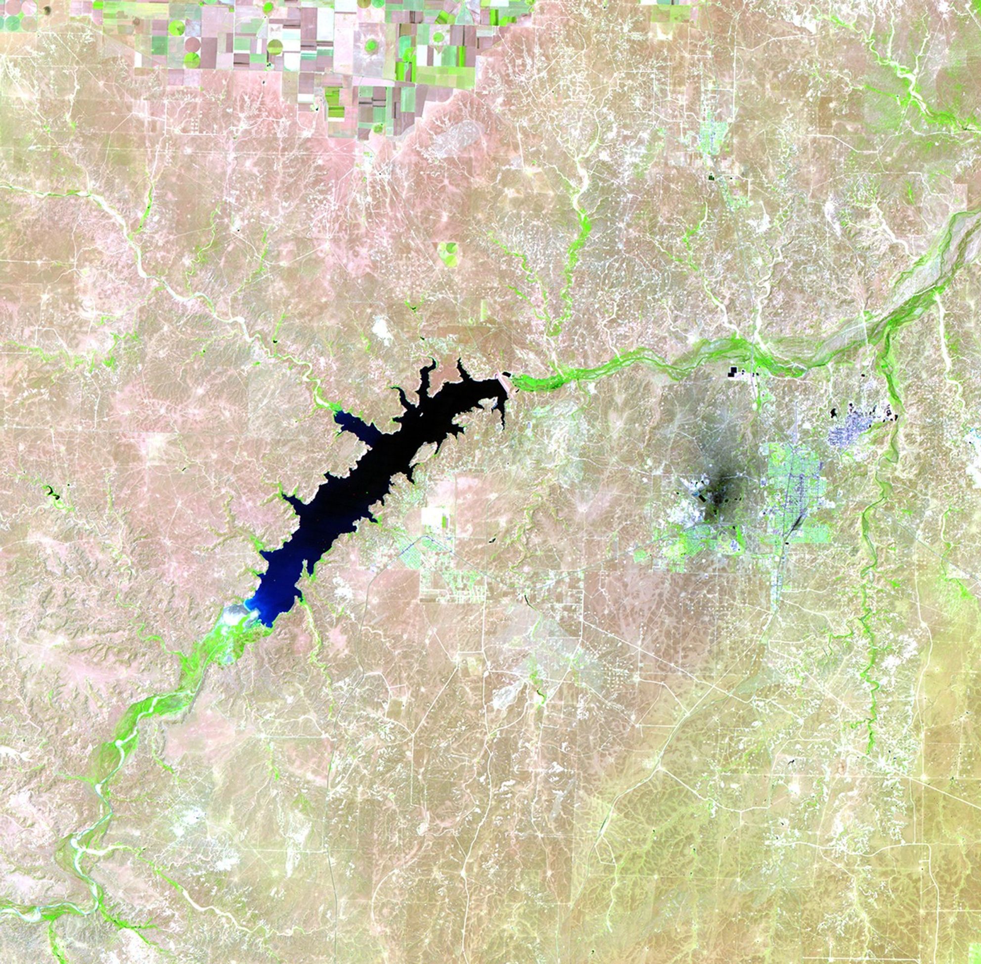Lake Meredith is a reservoir formed by the Sanford Dam on the Canadian River in the Texas panhandle. Continuous drought has diminished water levels significantly in the past few years, leading to a record low in 2011. In each image, the lake is the black feature near the center. Light tones at the lower end of the lake indicate dry land and former shores. Bright green indicates healthy vegetation along the river beds and irrigated fields in the upper center of each image. The nearby industrial area (a petroleum plant and a carbon-processing plant) appears as a dark spot. The light blue tone further east is Borger, Texas. Images taken by the Thematic Mapper sensor aboard Landsat 5. Source: USGS Landsat Missions Gallery, "Shrinking Lake Meredith, Texas," U.S. Department of the Interior / U.S. Geological Survey.