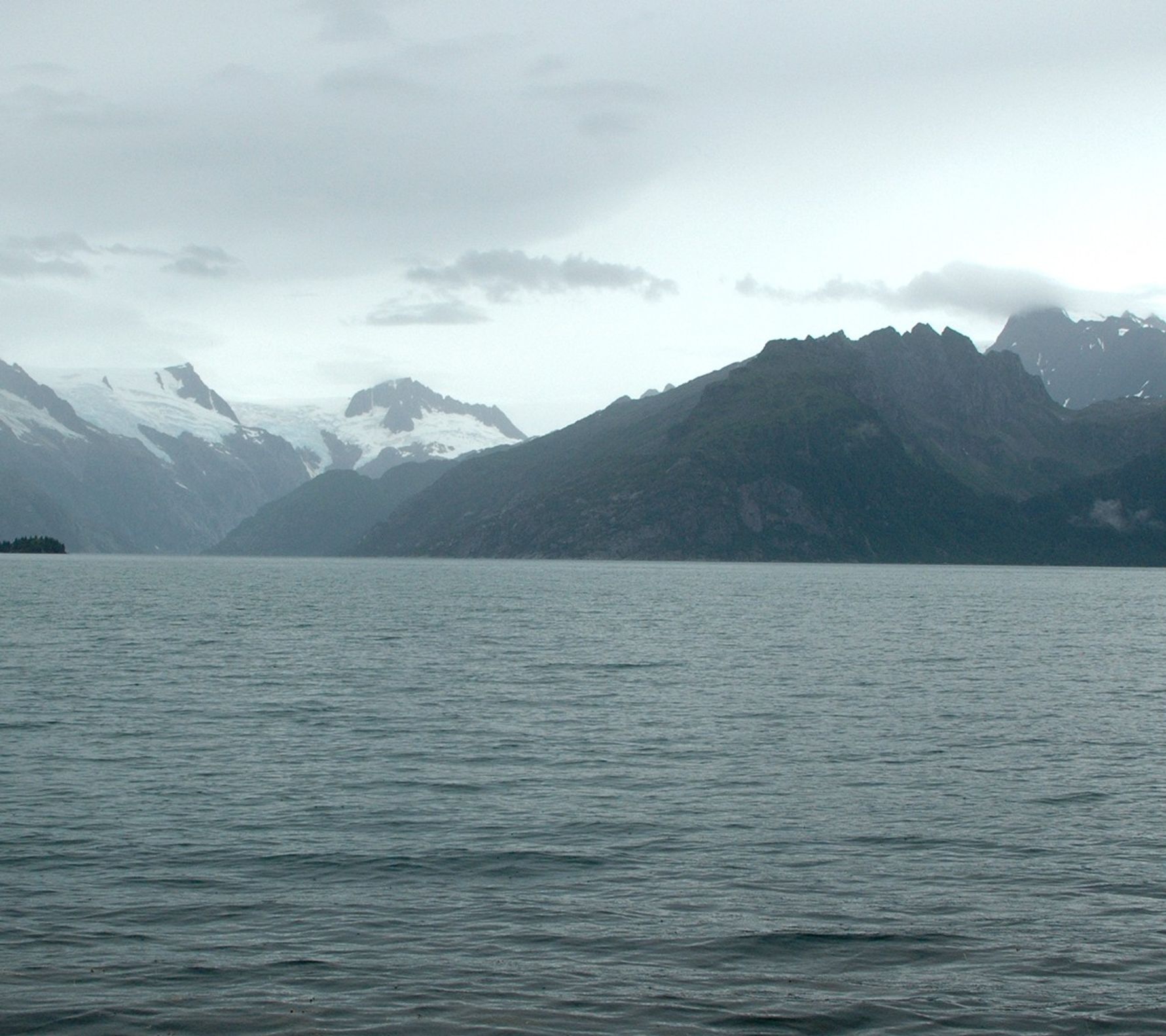 Looking north from the west shoreline of Harris Bay, Kenai Fjords National Park, Kenai Mountains, Alaska. The rocky shoreline in the foreground is covered by small icebergs, calved by the retreating Northwestern Glacier. During the roughly 60 to 80 years between photographs, Northwestern Glacier retreated some 6 miles (10 kilometers) to the northwest, out of the field of view.  U.S. Geological Survey, Department of the Interior. Earlier image is from a postcard, photographer unknown, courtesy of Kenai Fjords National Park. Later image is a USGS photograph by Bruce F. Molina.