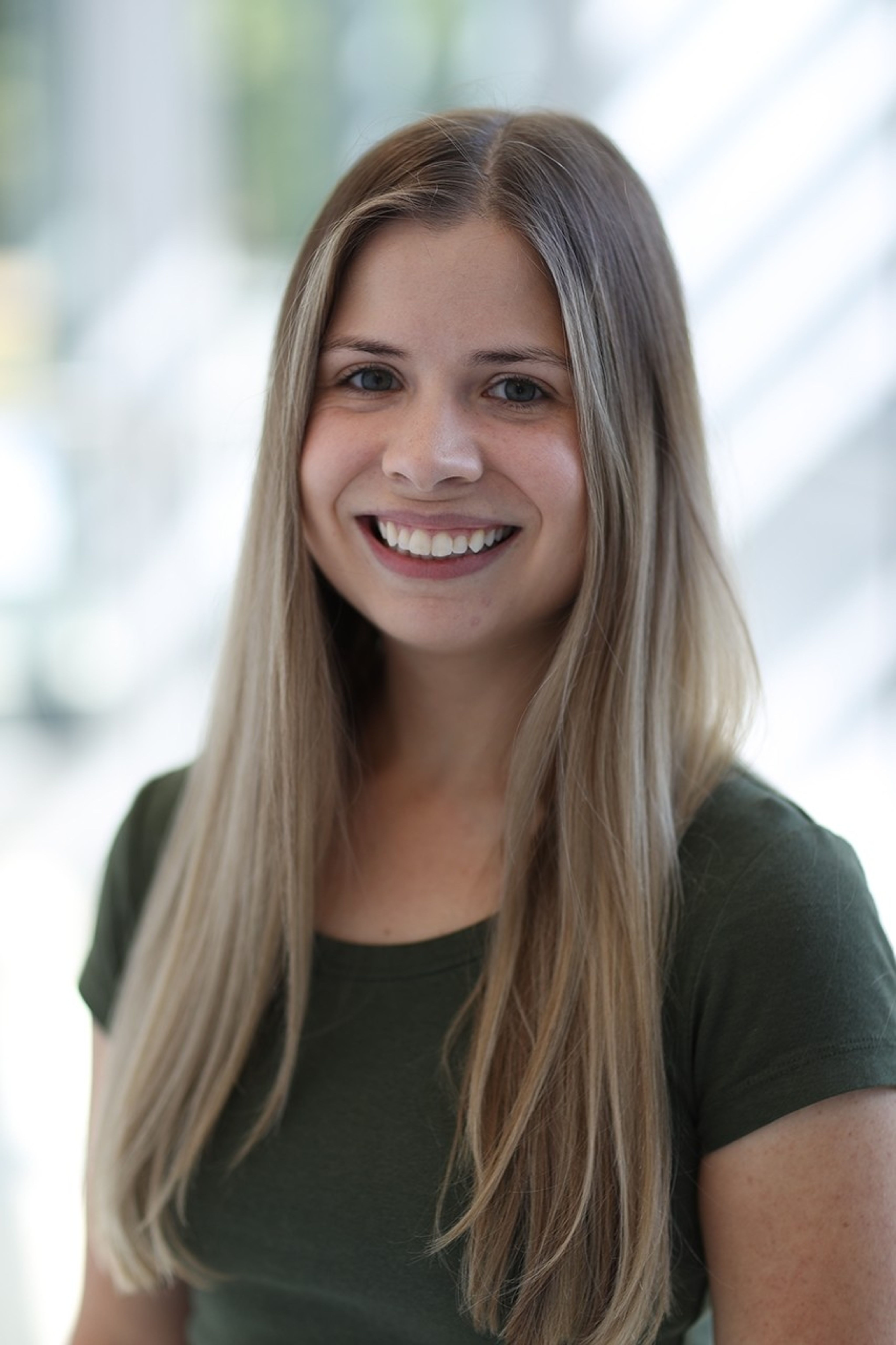 A woman with long dark blonde hair and a green t shirt. She is smiling at the camera.