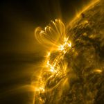 A portion of the Sun appears in shades of gold and black. In the upper left, several gold-shaded arches rise above a bright region on the Sun.