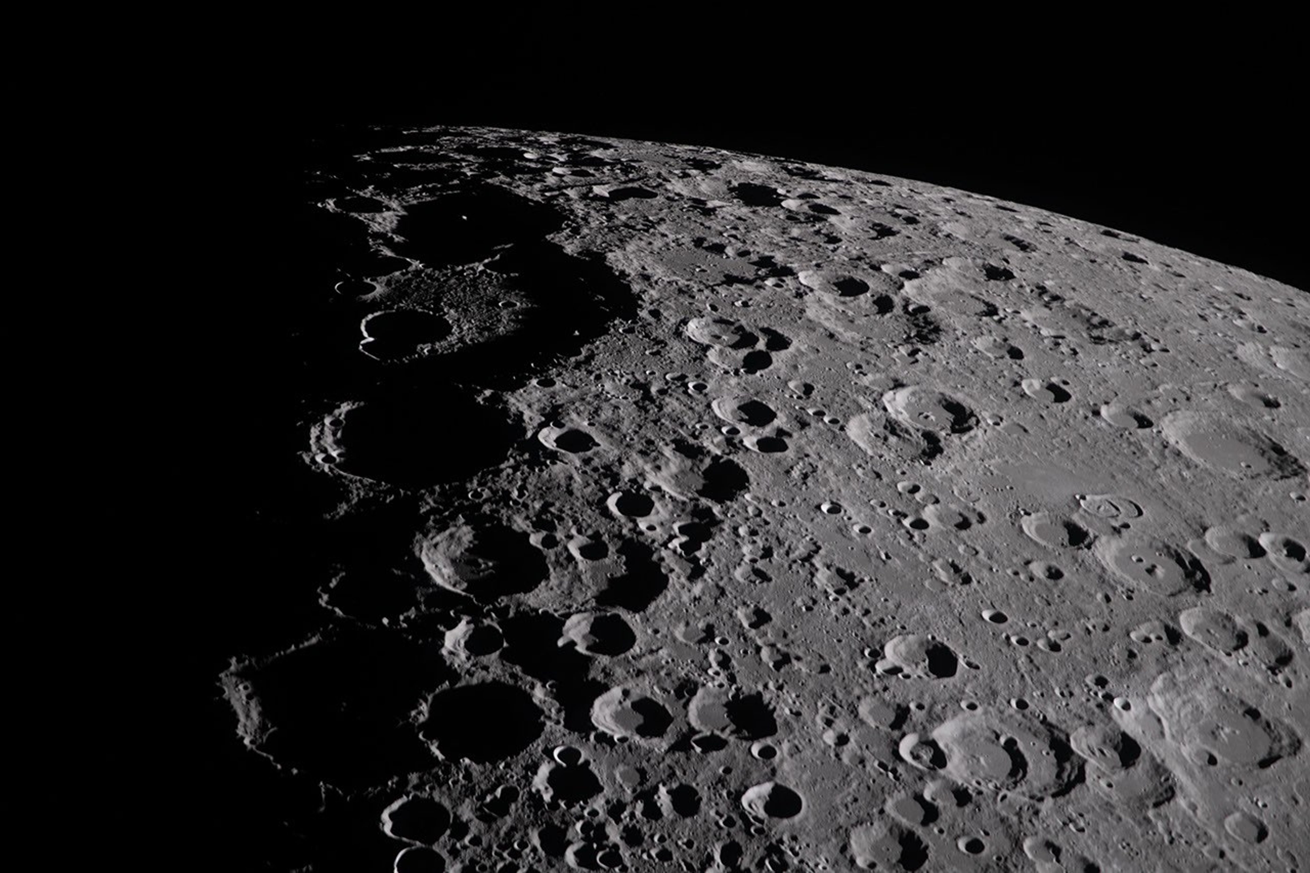 Una imagen de la superficie de la Luna a lo largo de su terminador. La vista se dirige hacia el borde de la Luna en la parte superior de la imagen, con el negro del espacio visible más allá. La superficie de la Luna está completamente cubierta de cráteres, cuyos centros se encuentran en profunda sombra. El terminador divide el lado nocturno de la Luna del lado diurno.
