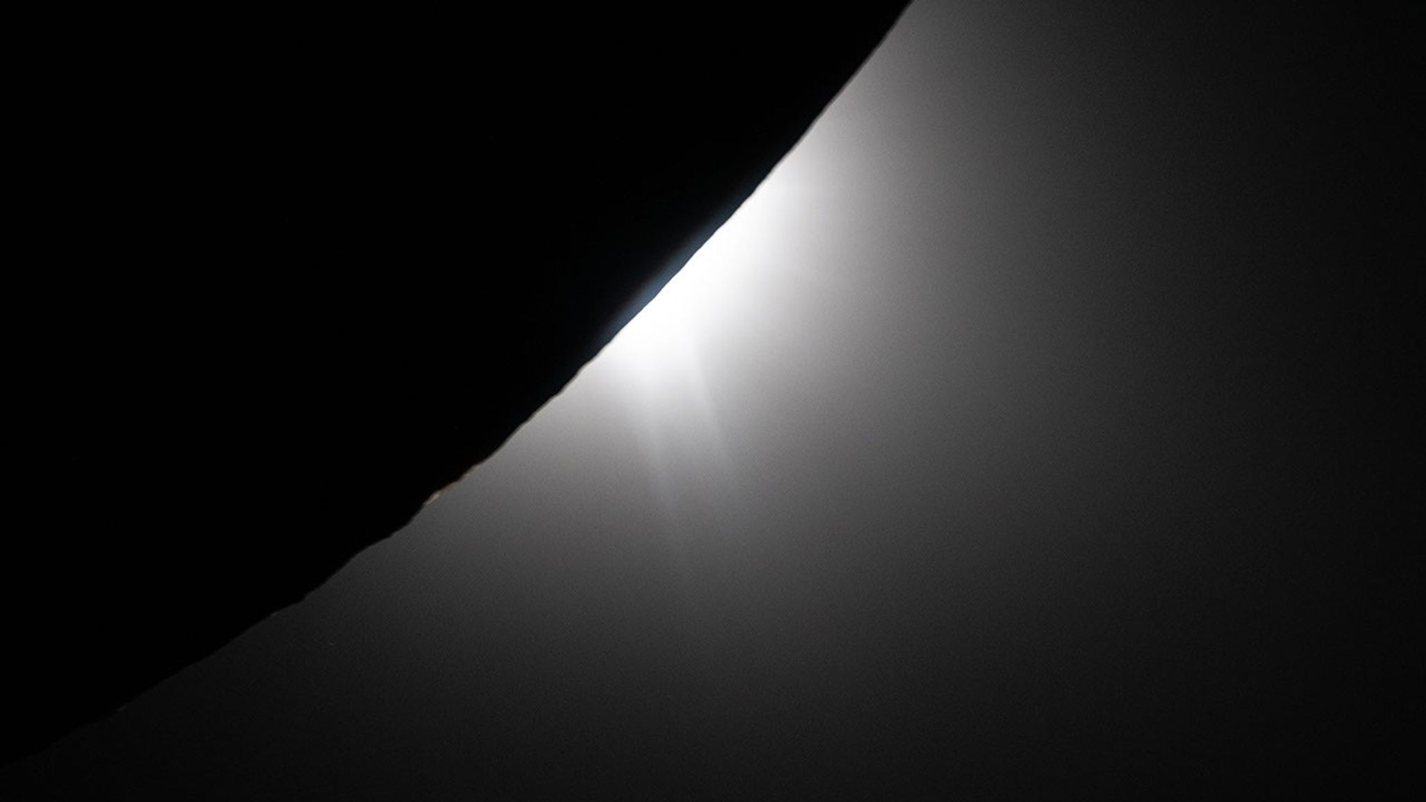 La Luna ocupa la esquina superior izquierda y es completamente negra. Detrás de la Luna, el Sol apenas es visible, pero un brillante resplandor blanco de luz solar irradia más allá de la superficie lunar. El resplandor ilumina el borde de la Luna. Este efecto muestra crestas, depresiones y protuberancias en la superficie lunar.