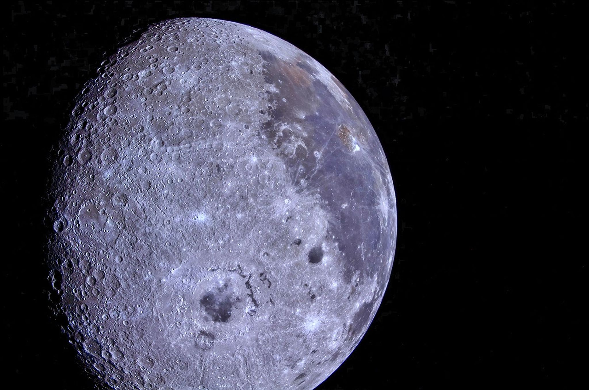 Vista de la Luna con colores realzados, contra el fondo negro del espacio, que muestra un terreno densamente cubierto de cráteres a la izquierda y llanuras más oscuras y lisas con tonalidades de azul, morado y marrón a la derecha. Las sombras resaltan los bordes de los cráteres a lo largo del margen izquierdo.