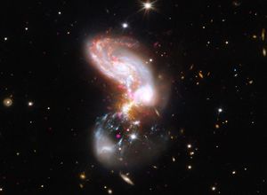 A chaotic, dust-shrouded system of merging galaxies forming stars at a furious rate. Chandra X-ray data (magenta) pinpoint powerful black hole activity and hot gas, while Hubble optical (blue and white) and Webb infrared (red and grey) data illuminate vast stellar nurseries hidden behind interstellar dust. Systems like II Zw 096 show us how powerful galaxy collisions shaped the early universe.