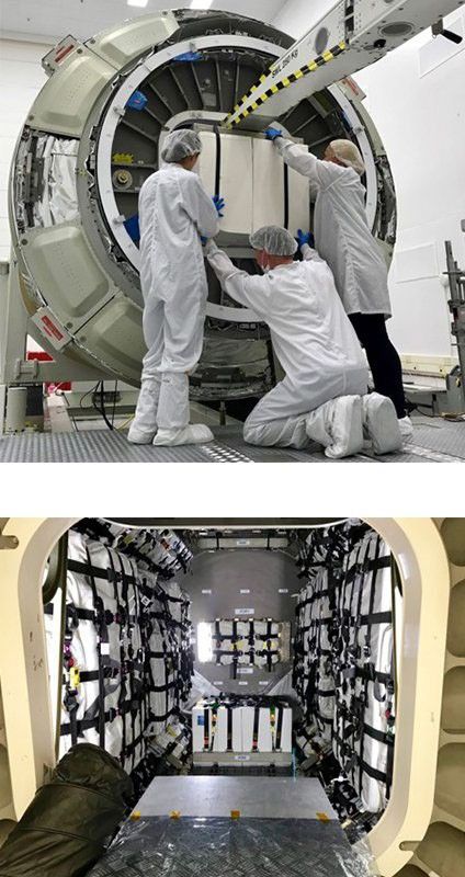 A two-panel image showing spacecraft cargo operations. The top panel shows three technicians in white cleanroom suits and hairnets loading a large, rectangular white payload into a cylindrical spacecraft module. The module's hatch is open, revealing its interior, and a yellow and black striped crane arm assists with the loading. The bottom panel shows the interior of a cargo bay, possibly a different section or a separate spacecraft, fully loaded with white bags secured by black netting and straps, with a central aisle for access. Some bags are also visible on a platform in the foreground.