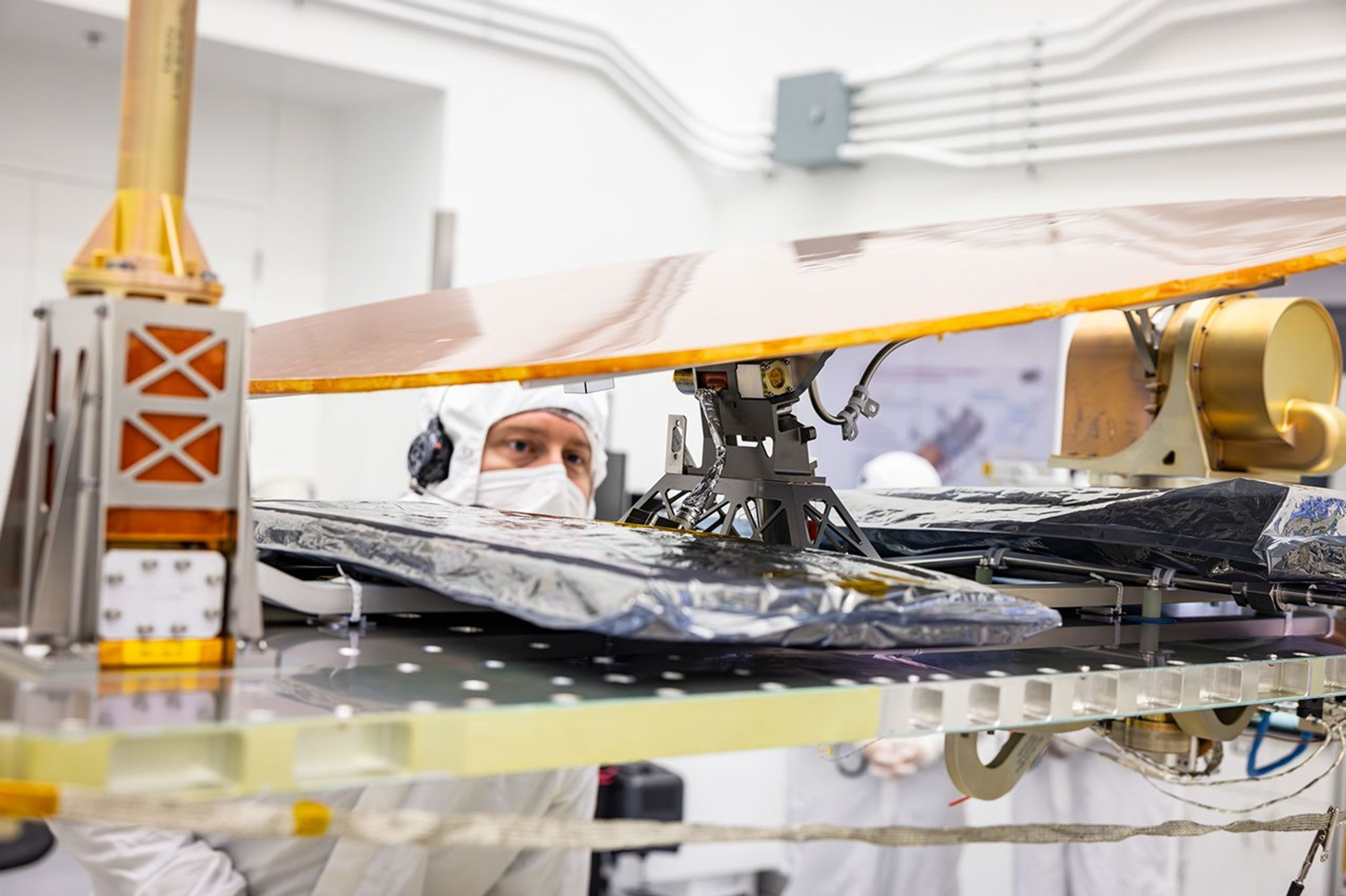 A technician in clean-room garments inspects Dragonfly’s golden high-gain antenna and its locking mechanism during spacecraft integration.