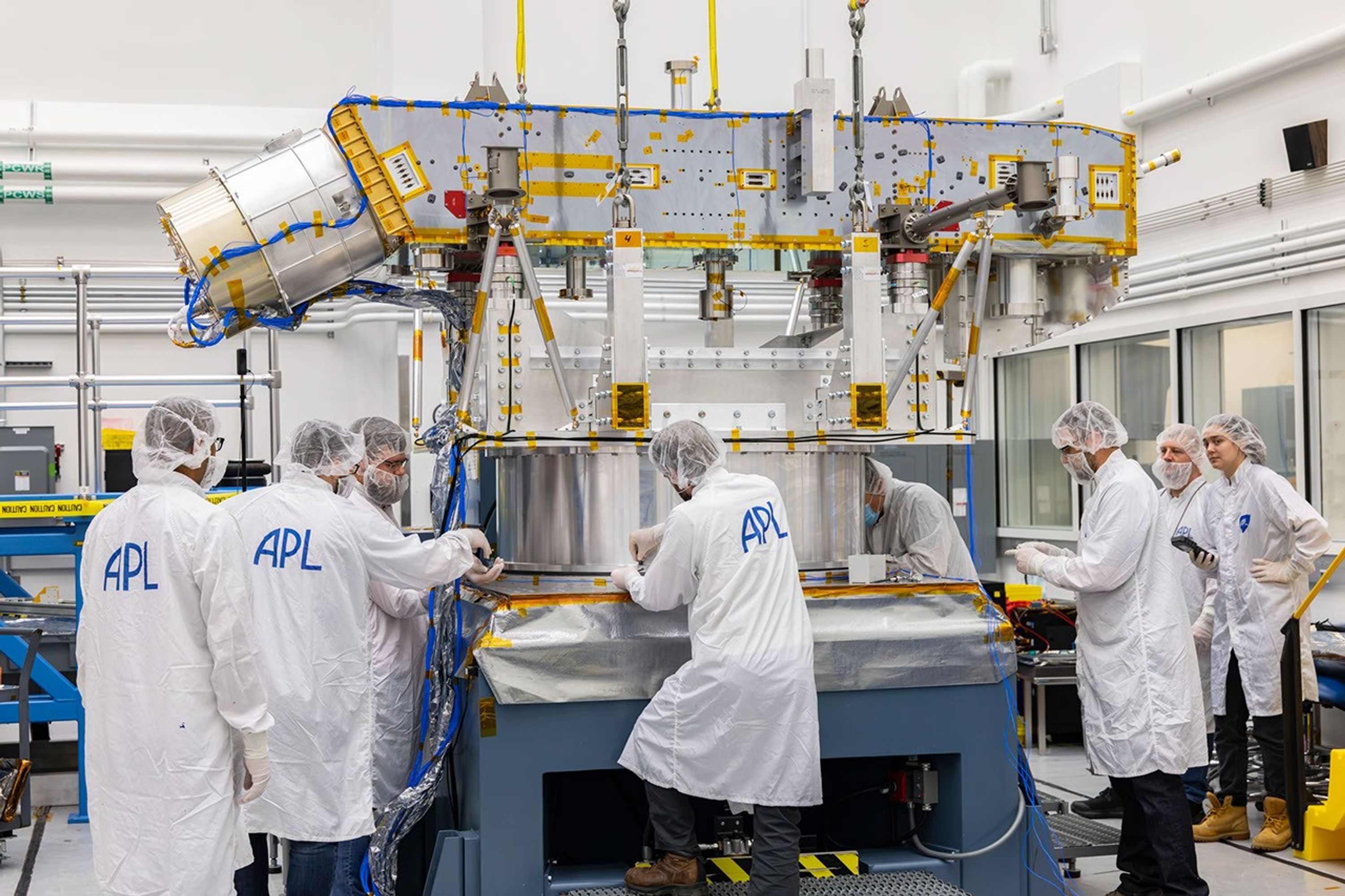 Engineers in cleanroom garments guide Dragonfly’s lander frame assembly onto a vibration test table.
