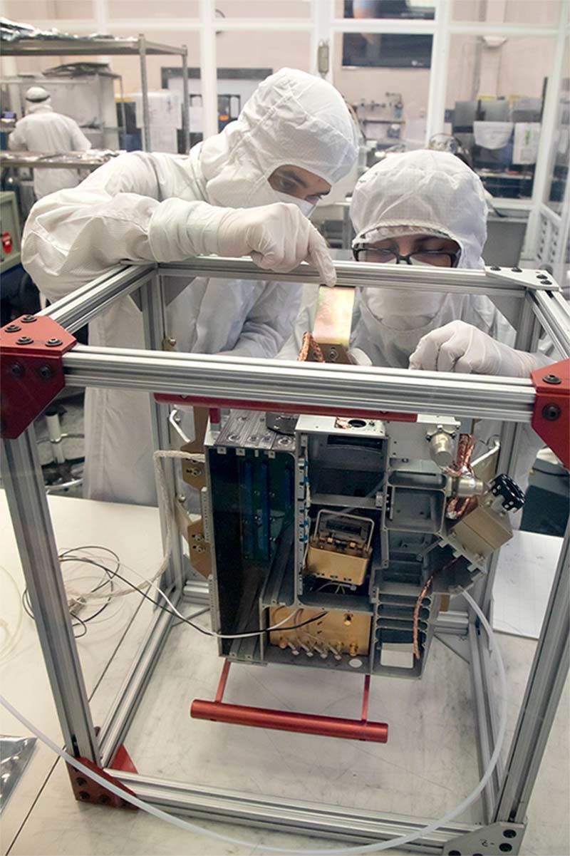Southwest Research Institute (SwRI)’s Brandon Perez (mechanical engineer; left) and Bryan Esquivel (technician; right) prepare to install electrical boards into the Europa Ultraviolet Spectrograph (Europa-UVS) instrument, tipped up to show a top view.