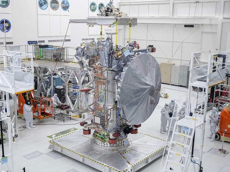 Europa Clipper's high gain antenna, which is taller than the nearby workers, is covered in a protective shroud as it sits on a platform at NASA's Jet Propulsion Laboratory.
