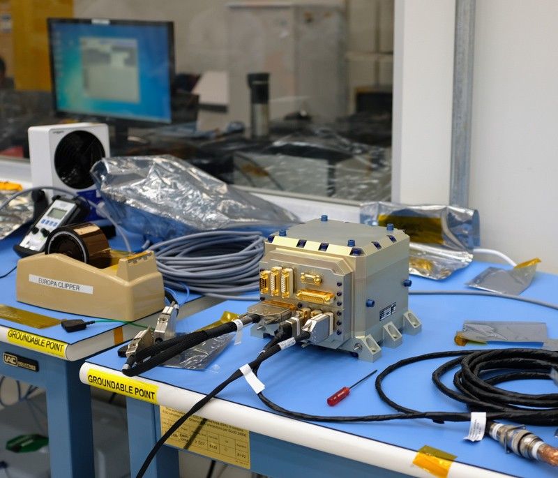In a clean room at NASA’s Jet Propulsion Laboratory, Mana Salami, guidance and control (G&C) systems engineer (front left) and Herrick Chang, cognizant engineer (front right), discuss testing for Europa Clipper’s star tracker. At far left is G&C hardware engineer Gabrielle Massone. At far right sits quality assurance engineer Shaunessy Grant. Chang, Massone, Grant, and James Alexander (not pictured) escorted the hardware from the Sodern company in France to JPL.