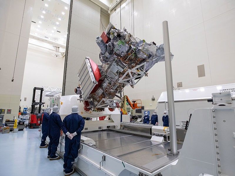 Workers in blue overalls and white head covers watch as equipment is used to rotate Europa Clipper.