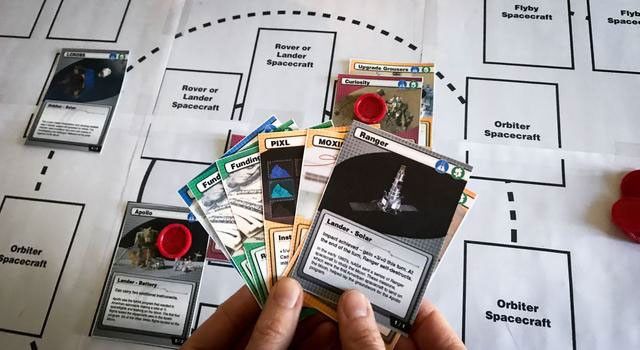 A person holding playing cards over a game board.