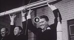 This iconic black-and-white historic photograph captures William Pickering, James Van Allen, and Wernher von Braun triumphantly holding a full-scale model of the Explorer 1 satellite above their heads during a press conference at the National Academy of Sciences. The three men are smiling broadly as they celebrate the successful launch of America's first satellite on January 31, 1958. In the background, an inscription on the stone wall is partially visible, while a smaller rocket model stands on a table in the lower right corner, symbolizing the beginning of the U.S. space age.