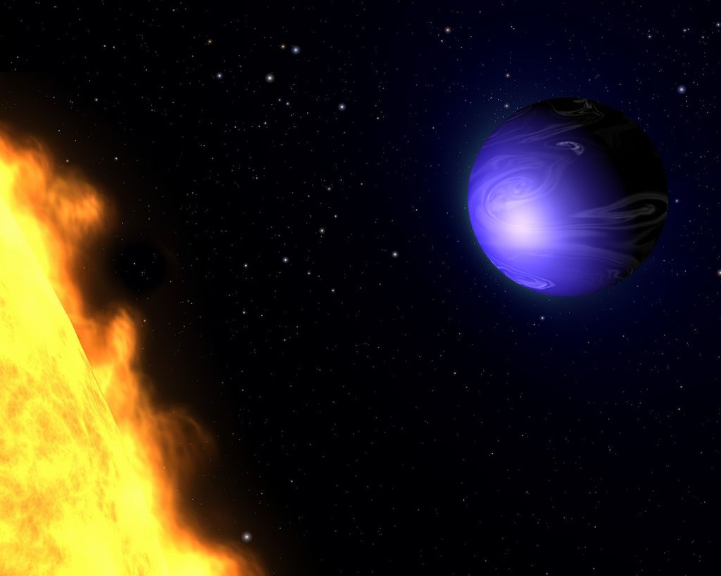 In the upper-right is an indigo sphere of a planet covered with light purple swirls of clouds, resembling a marble. In the lower left is the arc of one small portion of the planet's star, appearing mostly yellow with orange patches and plasma radiating from it. All against a black backdrop of space with multicolored stars.