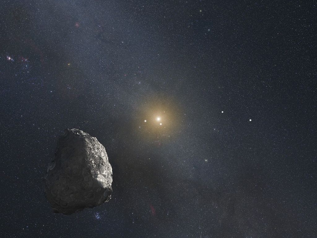 The Sun glows in the center of the image as a small but bright yellow star. In the bottom-left quadrant in the foreground is a rocky, gray, asteroid-shaped Kuiper Belt Object. In the background, the vastness of space appears salt-and-pepper, almost hazy white, thanks to the presence of so many stars.