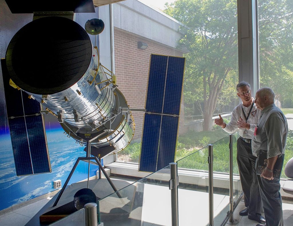 Jim Jeletic and Bill Anders stand to the right side of the photo, with Jeletic (on the left) talking to Anders (on the right). On the left side of the image is the Hubble model.