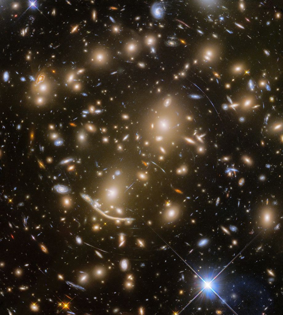 A field of galaxies along with the curved arcs of gravitationally lensed galaxies.