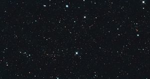 Image is filled with distant galaxies in colors of yellow-gold, red, blue, white.