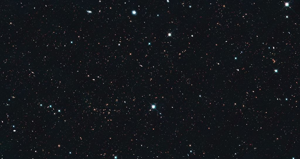 Image is filled with distant galaxies in colors of yellow-gold, red, blue, white.