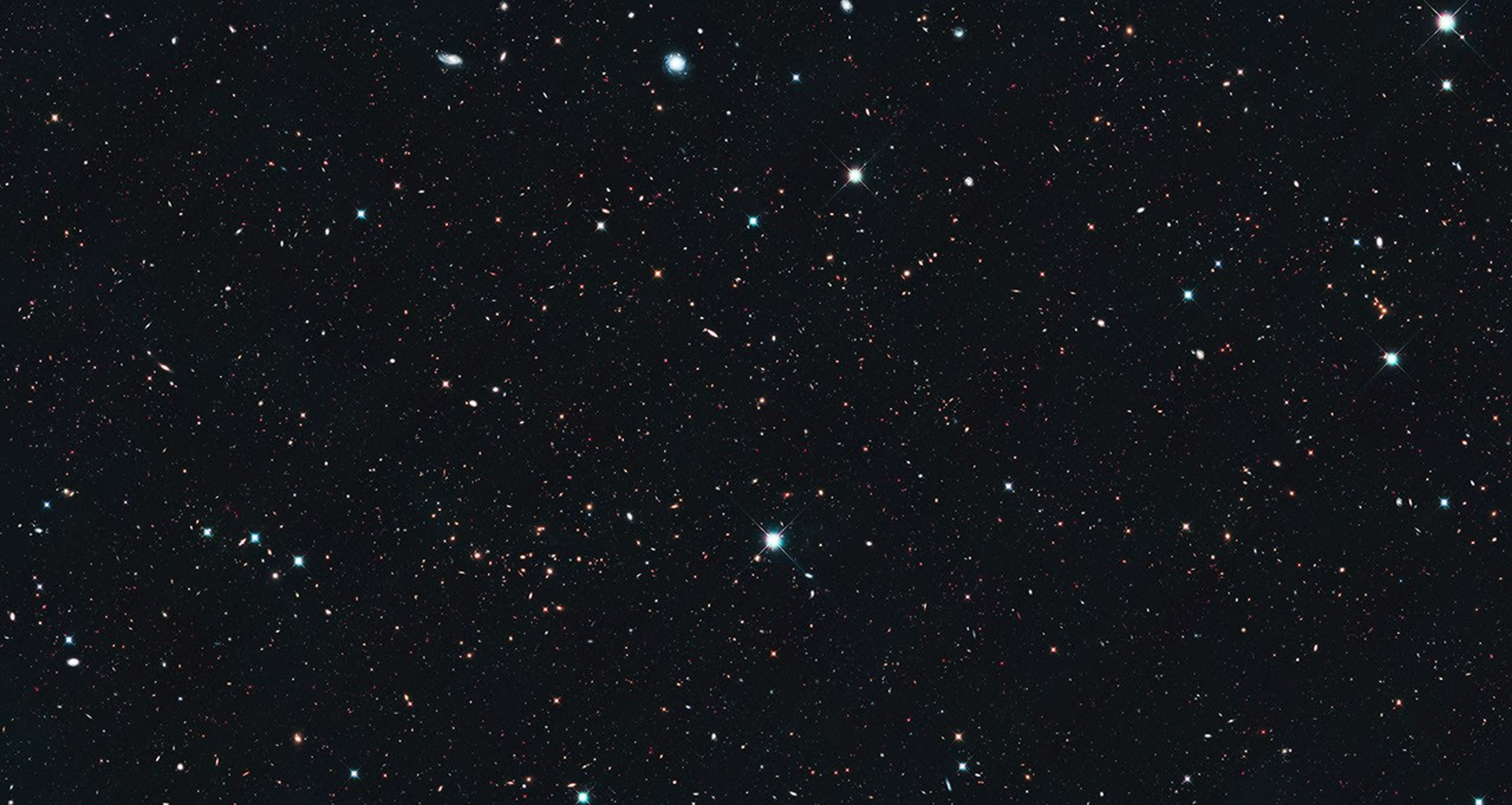 Image is filled with distant galaxies in colors of yellow-gold, red, blue, white.