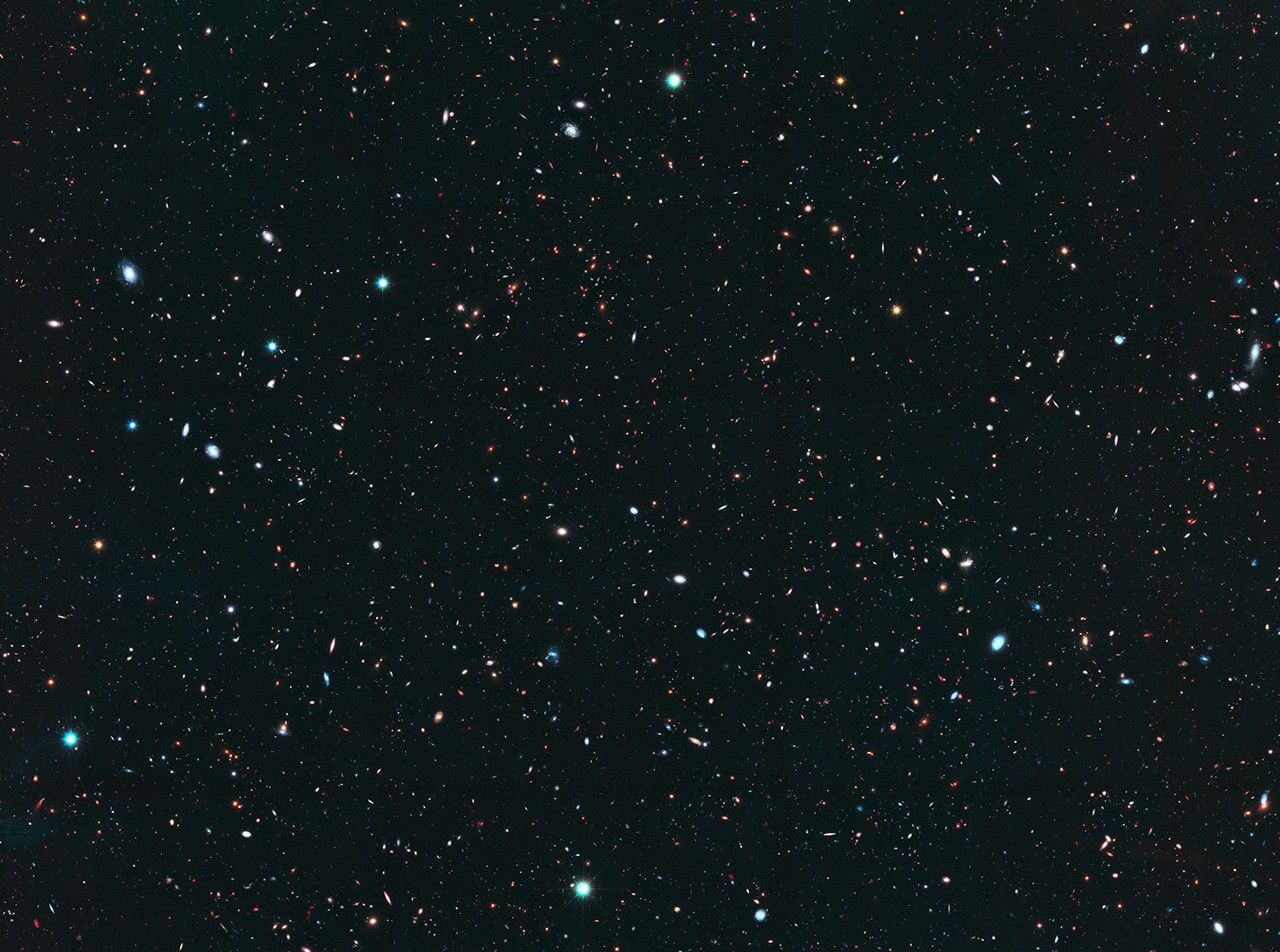 Image is filled with distant galaxies in colors of yellow-gold, red, blue, white. Many of the stars and galaxies have a bluish tint.
